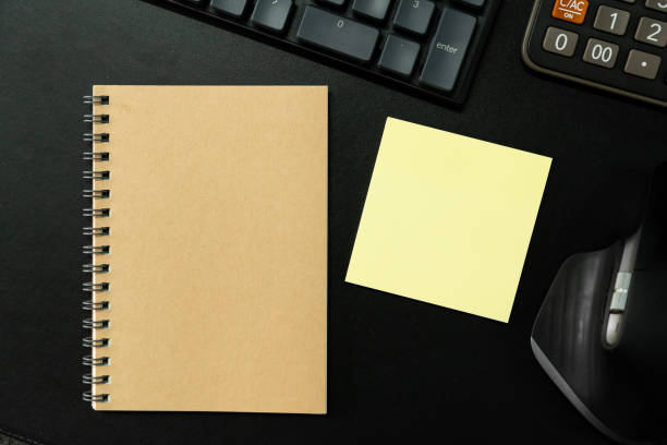 Top view of notebook. Blank paper notepad on office desk table with keyboard and other supplies. Blank notebook page for input the text. copy space, flat lay.