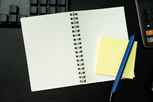 Top view of notebook. Blank paper notepad on office desk table with keyboard and other supplies. Blank notebook page for input the text. copy space, flat lay.