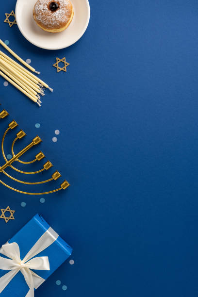 istock A beautiful Hanukkah vertical arrangement featuring a menorah, candlesticks, a powdered doughnut, and a gift box on a blue surface, creating a festive celebration atmosphere 2184680982