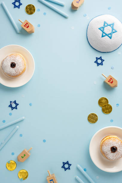 istock Top vertical view of a Hanukkah celebration table with dreidels, donuts, and coins on a light blue background 2184680985