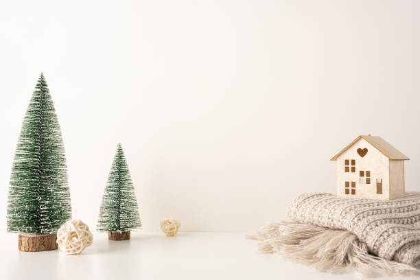 istock Minimalist Scandinavian Christmas side view scene featuring miniature snow-covered trees and a wooden house on a cozy knit blanket 2184681123