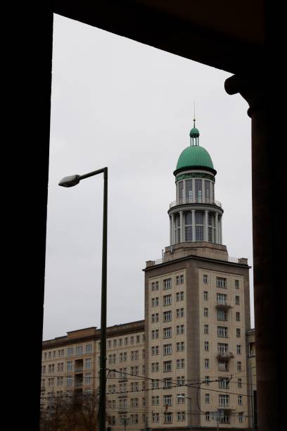 View of a historic building with a green dome in Berlin, framed by an archway on a cloudy day.