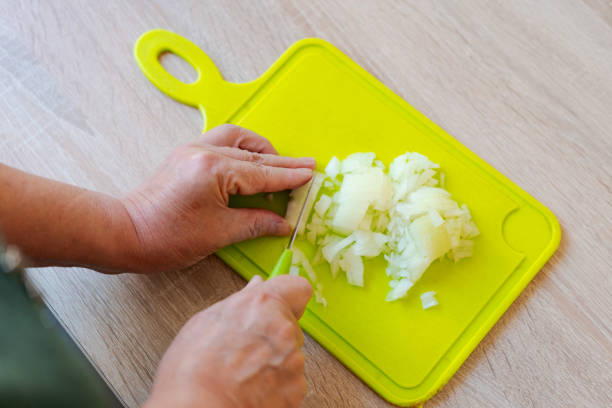 Person is cutting onions on a green cutting board. The onions are being chopped into small pieces