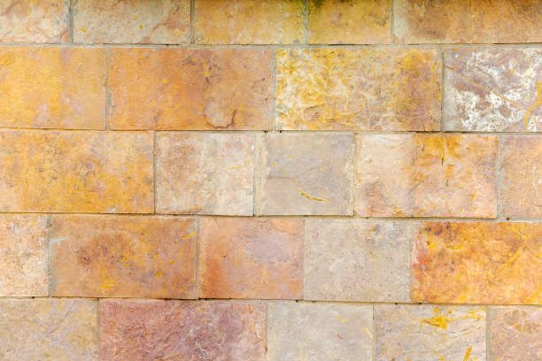 Brick wall with a yellow and brown color. The wall is made of bricks and has a rough texture