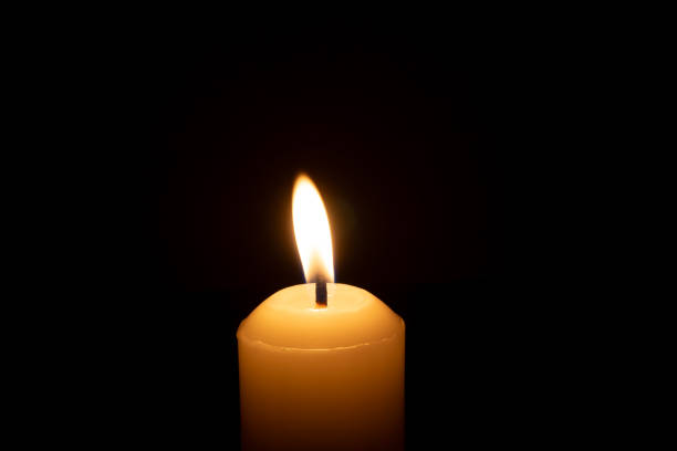 istock A single burning candle flame or light glowing on a big white candle isolated on black or dark background on table in church for Christmas, funeral or memorial service 2184691682