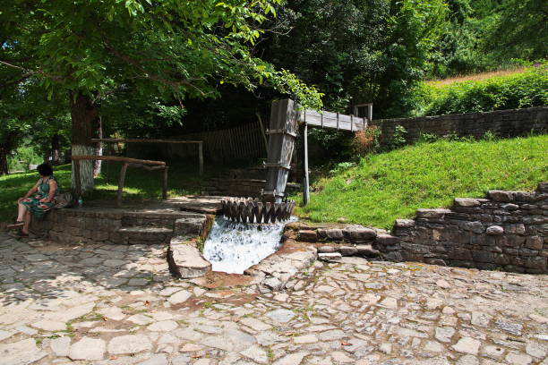 A picturesque scene of the historic Tapolca watermill with a cascading waterfall and colorful koi fish swimming in the clear waters below. The lush greenery and soft light highlight the town’s charming and peaceful atmosphere.