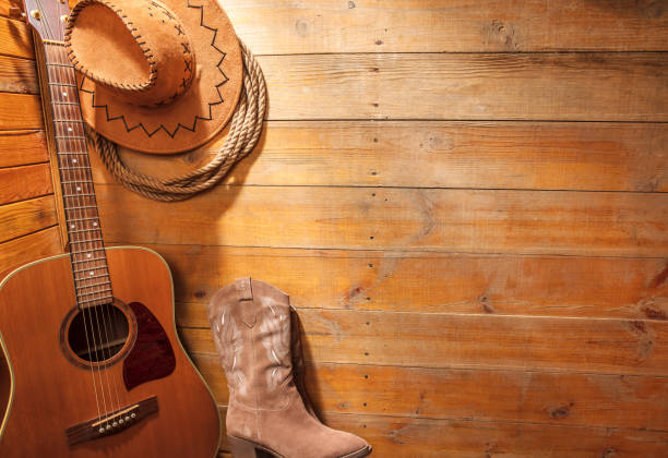 Acoustic guitar, lasso, cowboy hat and boots on a barn wood texture background. American Country music concept. Space for copy.