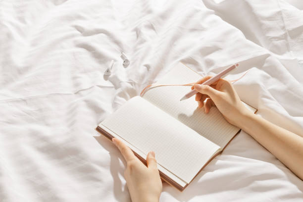 istock Woman takes notes or makes plan, day results on blank white page of paper in notebook or diary, holds notepad and pen in hands, top view, time for yourself morning or evening before sleep 2184695690