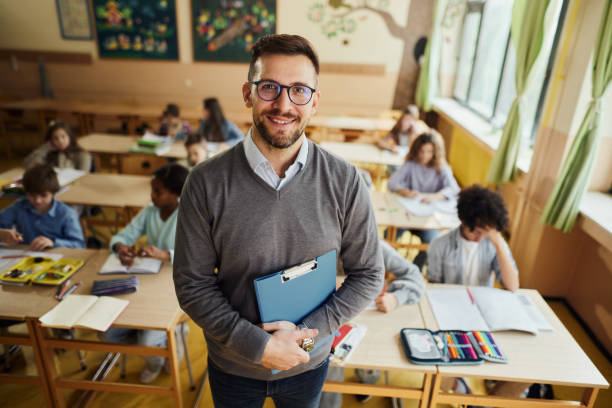 istock Happy elementary teacher in front of his students in the classroom. 2184696855