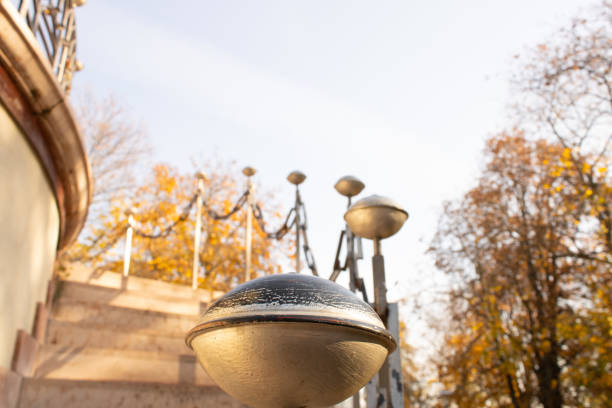 A decorative golden railing with an autumn backdrop of vibrant yellow and orange foliage. The sunlight highlights the intricate details of the metalwork.