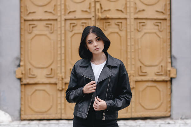 portrait of beautiful young caucasian woman looking confidently, street background, black hair, black leather jacket