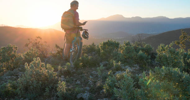 istock Mature mountain biker uses mobile phone on hill at sunrise 2184701661