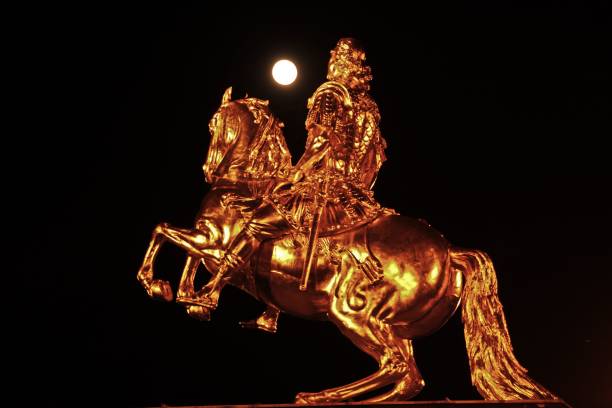 Golden equestrian statue against a dark night sky with a full moon, showcasing intricate details and dramatic lighting.