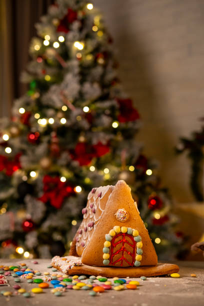 A gingerbread house made at home with sweet decorations, Christmas tree in the background.