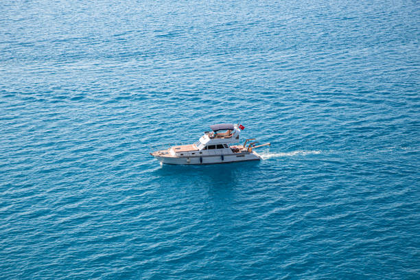 A minimalist coastal scene along the Great Ocean Road, Australia. The image captures an endless expanse of deep blue ocean under a soft sky, with a tiny fishing boat carrying two people at the center. The small vessel appears almost lost in the vast seascape, conveying a sense of solitude, scale, and tranquility. Perfect for concepts of adventure, freedom, and the power of nature.