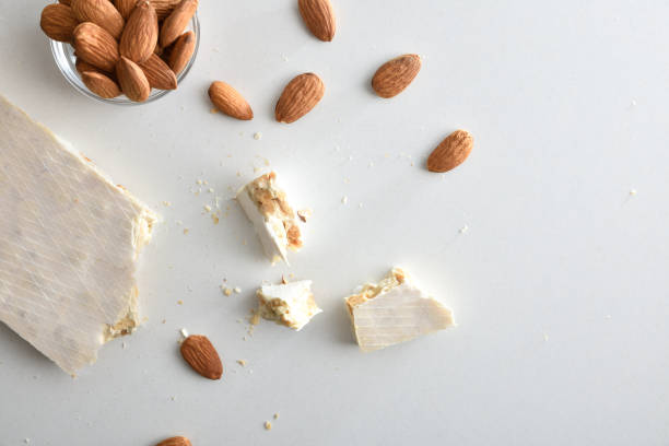 Almond nougat tablet with honey and sugar and wafer coating and bowl with natural almonds isolated on white table. Top view.
