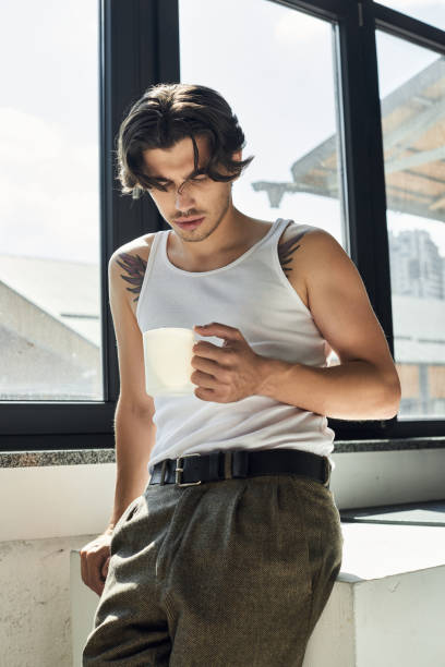 A stylish young man poses with a cup in a bright, modern studio