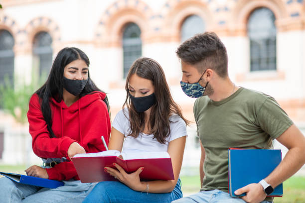 istock College students wearing protective face masks studying together outdoors 2184725830
