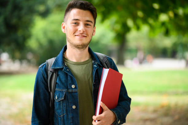 istock Smiling university student holding books and walking in a park 2184728090