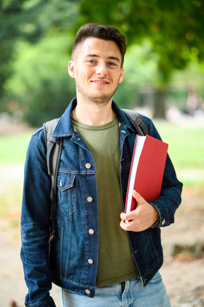 istock Smiling university student holding a book and wearing a backpack 2184728326