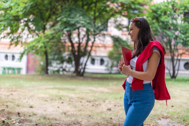 istock Young student holding books and smiling in university campus park 2184728662