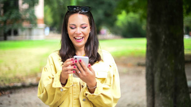 istock Young woman laughing while using smartphone in a park 2184729506