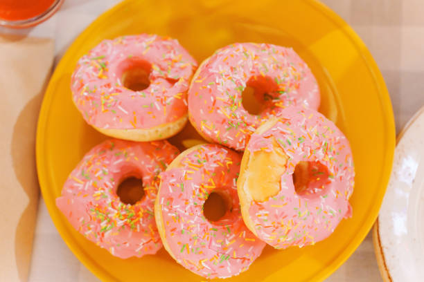 istock donuts covered with pink icing on a yellow plate. 2184731367