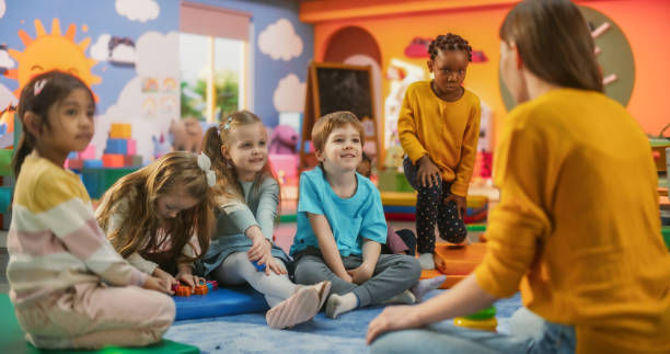 istock Happy Kindergarten Pedagogue Having a Conversation with Kids, Using Enthusiastic Teaching Methods in a Modern Colorful Kindergarten. Female Educator Stimulating Linguistic and Social Skills 2184734791