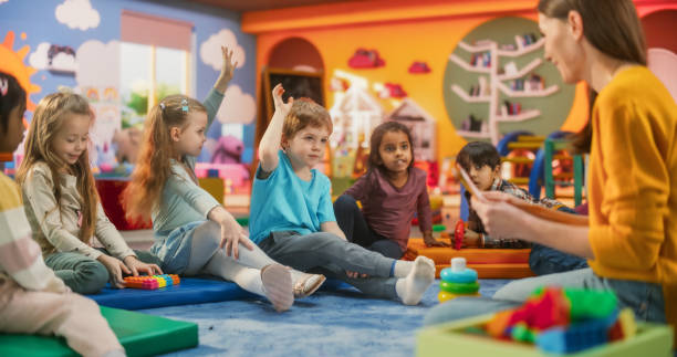 istock Happy Kindergarten Pedagogue Having a Conversation with Kids, Using Enthusiastic Teaching Methods in a Modern Colorful Kindergarten. Female Educator Stimulating Linguistic and Social Skills 2184734831