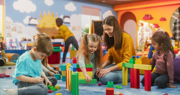 istock Happy Kindergarten Pedagogue Having a Conversation with Kids, Using Enthusiastic Teaching Methods in a Modern Colorful Kindergarten. Female Educator Stimulating Linguistic and Social Skills 2184735043