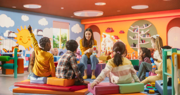 istock Cheerful Preschool Educator Playing and Creatively Studying with Multiethnic Kids in Kindergarten. Small Adorable Children Getting Basic Reading and Writing Skills, Learning Alphabet 2184738141