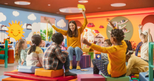 istock Cheerful Preschool Educator Playing, Singing and Dancing with Multiethnic Kids in Kindergarten. Small Adorable Children Learning and Having Fun 2184738170