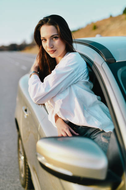 istock Beautiful Woman Looking at Camera Leaning on Open Car Window and Posing 2184739050