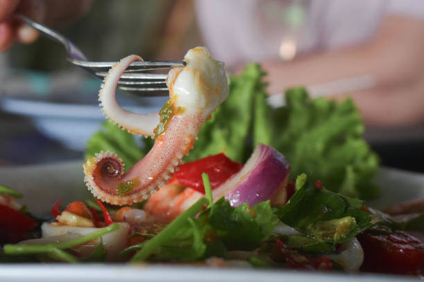 Seafood salad made with crispy calamari, sliced radish, exotic tomatoes and microgreens, served in an earth-toned bowl on a wooden restaurant table.