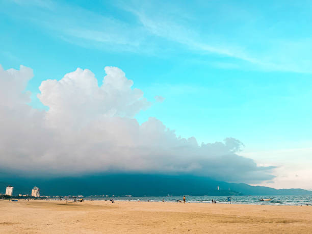 The serene morning paints the sky with vibrant shades of orange, pink, and purple, reflecting on the calm waters of My Khe Beach. Silhouettes of swimmers and fishing boats dot the tranquil coastline.