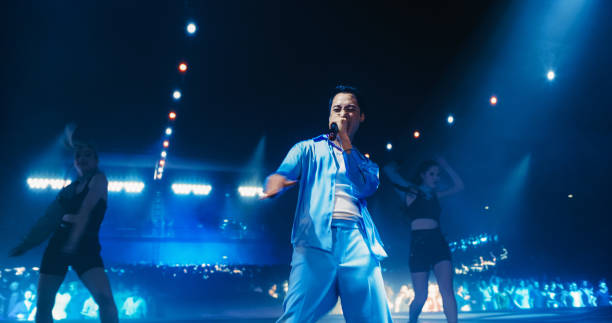 istock Fans Experiencing a Powerful Musical Performance by a Talented Asian Singer. Pop Band Lead Singer Works on Stage With a Blend of Emotion and Energy. Light Show and Skilled Dancers in the Background 2184747037