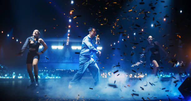 istock Fans Experiencing a Powerful Musical Performance by a Talented Asian Singer. Pop Band Lead Singer Works on Stage With a Blend of Emotion and Energy. Light Show and Skilled Dancers in the Background 2184747070
