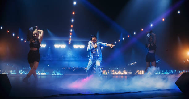 istock Fans Experiencing a Powerful Musical Performance by a Talented Asian Singer. Pop Band Lead Singer Works on Stage With a Blend of Emotion and Energy. Light Show and Skilled Dancers in the Background 2184747089