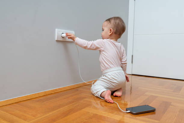 istock Curious toddler exploring an electric socket with a phone charger, highlighting the importance of home safety and parental vigilance. 2184748464
