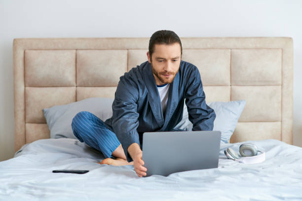istock A young man with a beard works on his laptop in bed during a calm morning 2184752122