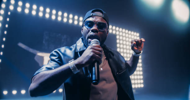istock Creative Rap Artist Performing a Hit Song on Stage with a Striking Female Dancer, Inspiring a Large Audience in a Colorful Neon Concert Setting with Cinematic Lighting and Animated LED Screen 2184753463