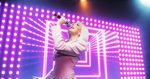 istock Fans Experiencing a Powerful Musical Performance by a Talented Young Singer. Beautiful Pop Band Lead Singer in Pink Clothes Works on Stage With a Blend of Emotion and Energy, Singing Songs to Audience 2184753764