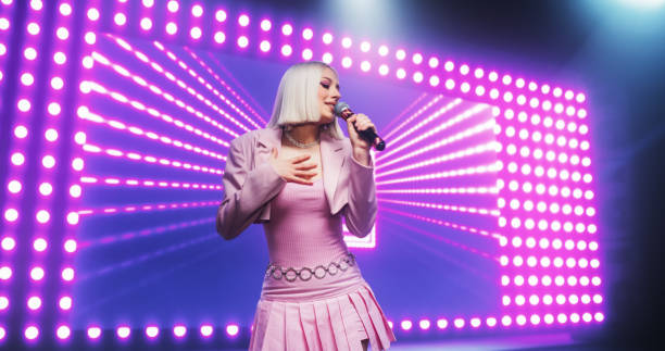 istock Fans Experiencing a Powerful Musical Performance by a Talented Young Singer. Beautiful Pop Band Lead Singer in Pink Clothes Works on Stage With a Blend of Emotion and Energy, Singing Songs to Audience 2184753796