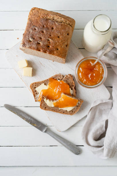 Whole grain bread with apricot jam on a white cutting board