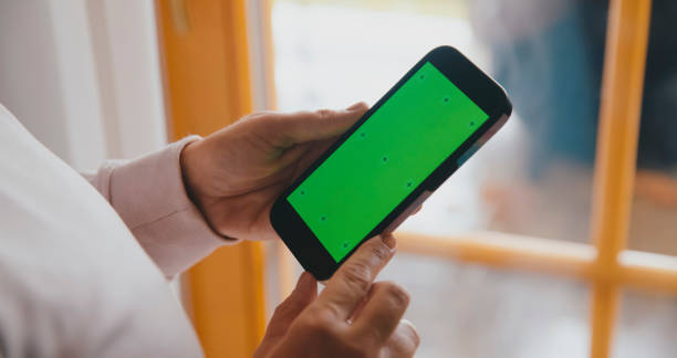 istock Person Engaged with Green Screen Smartphone by Window 2184756410