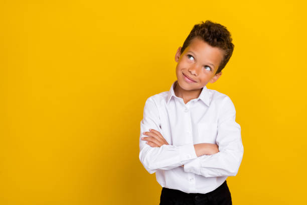 istock Photo of nice smart clever boy arm folded interested look up empty space choice choose consider dilemma isolated on yellow color background 2184756420