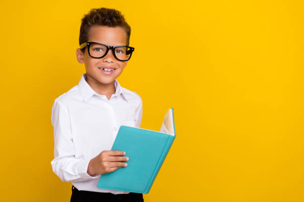 istock Photo of clever cute boy learner wear eyeglasses hold copybook read task question exercise empty space isolated on yellow color background 2184756433