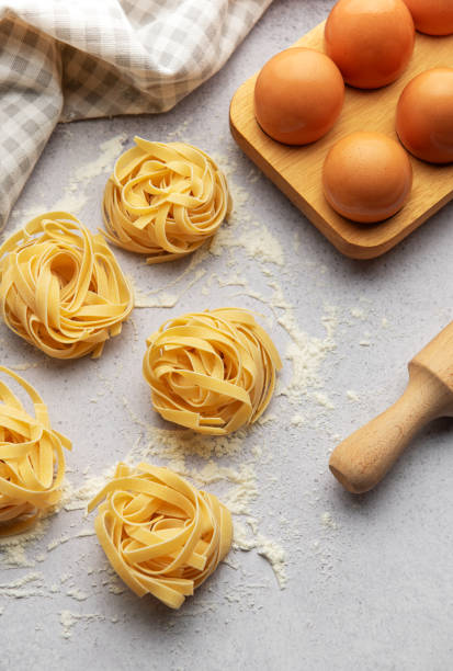 istock Tagliatelle nests with flour, eggs and rolling pin composing a beautiful food background 2184759228