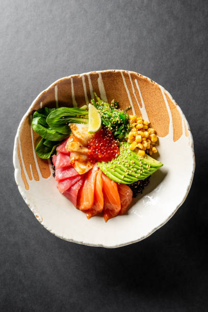 A bowl of poke with raw fish slices, avocado, corn, greens, and rice, garnished with sesame seeds. The vibrant colors and fresh ingredients make it a visually appealing and healthy meal option.