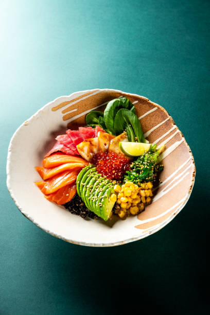 A bowl of poke with raw fish slices, avocado, corn, greens, and rice, garnished with sesame seeds. The vibrant colors and fresh ingredients make it a visually appealing and healthy meal option.